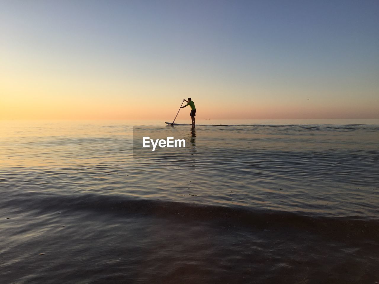 Silhouette man paddleboarding in sea against clear sky