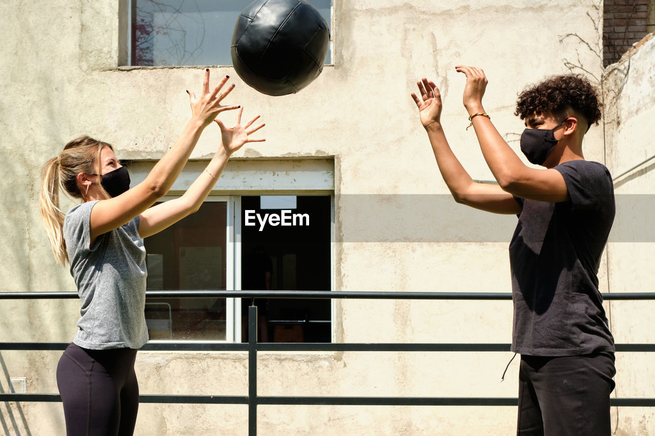 Couple wearing mask exercising with ball outdoors