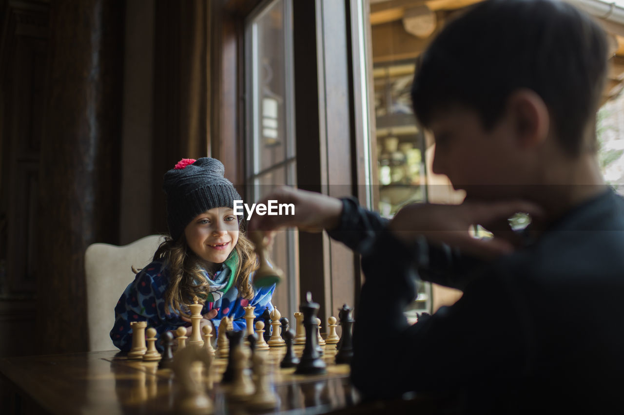 Siblings playing chess by window at home