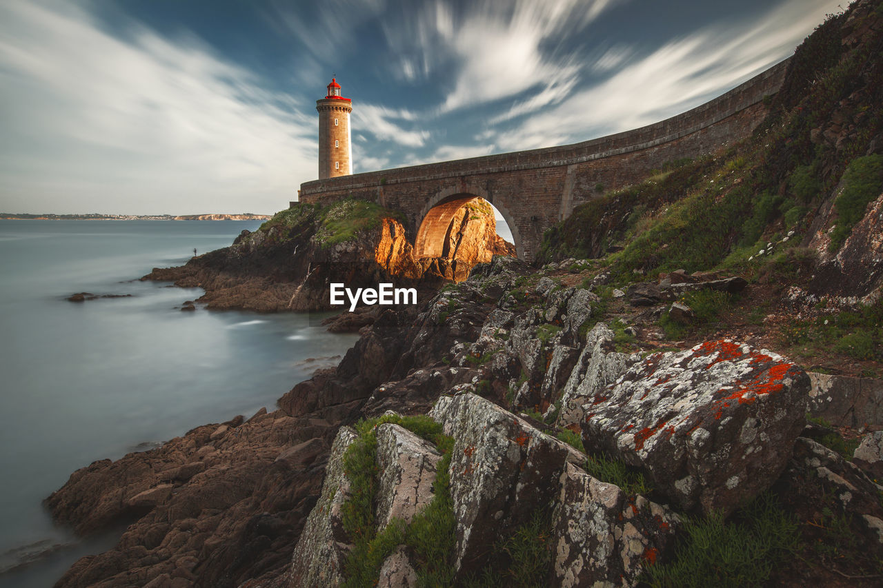 Lighthouse by building against sky