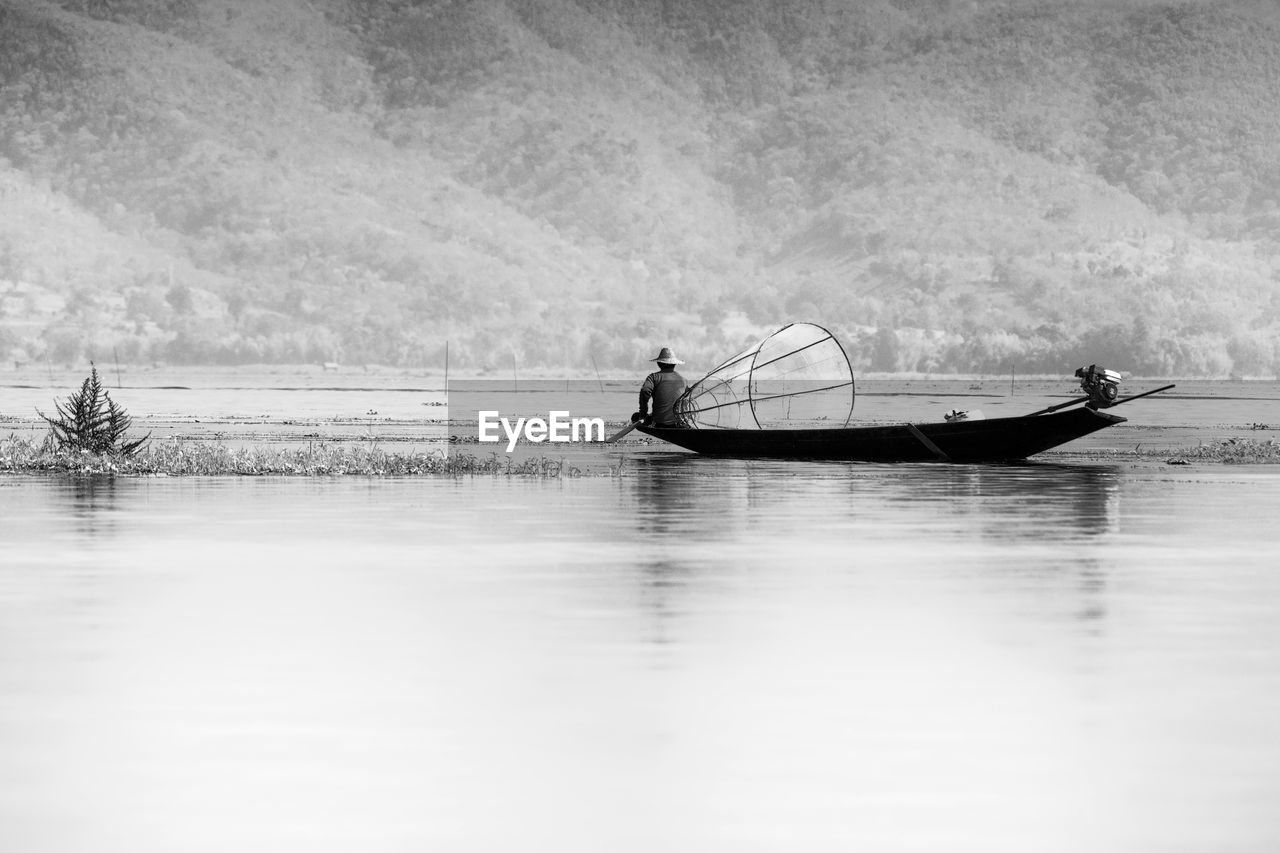 MAN IN BOAT ON LAKE AGAINST SKY