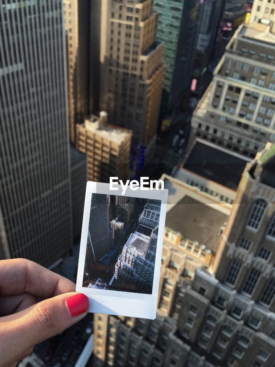 Close-up of female hand holding instant camera picture against buildings