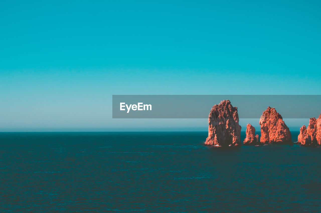 Scenic view of rock formation in sea against clear blue sky