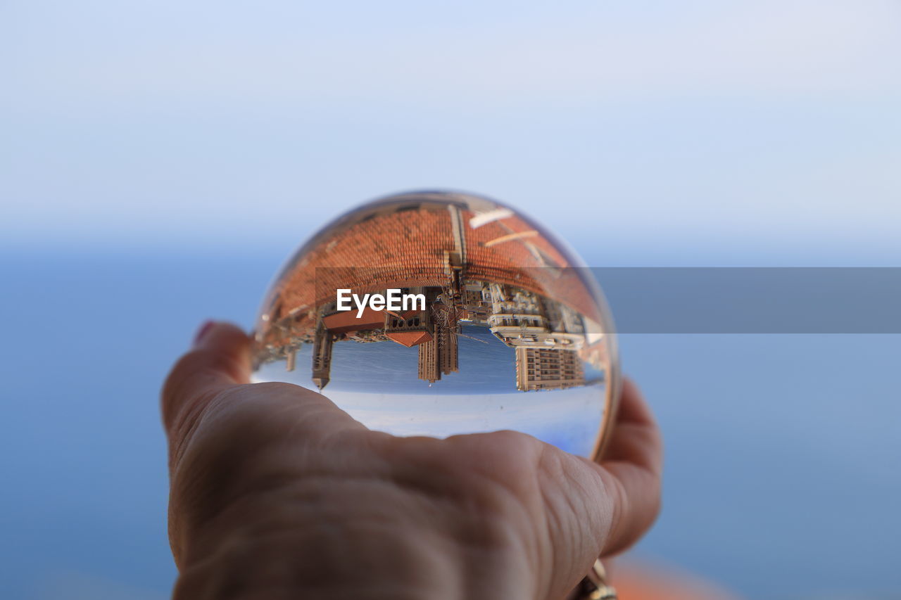 Cropped image of person holding glass ball with upside down reflection of town