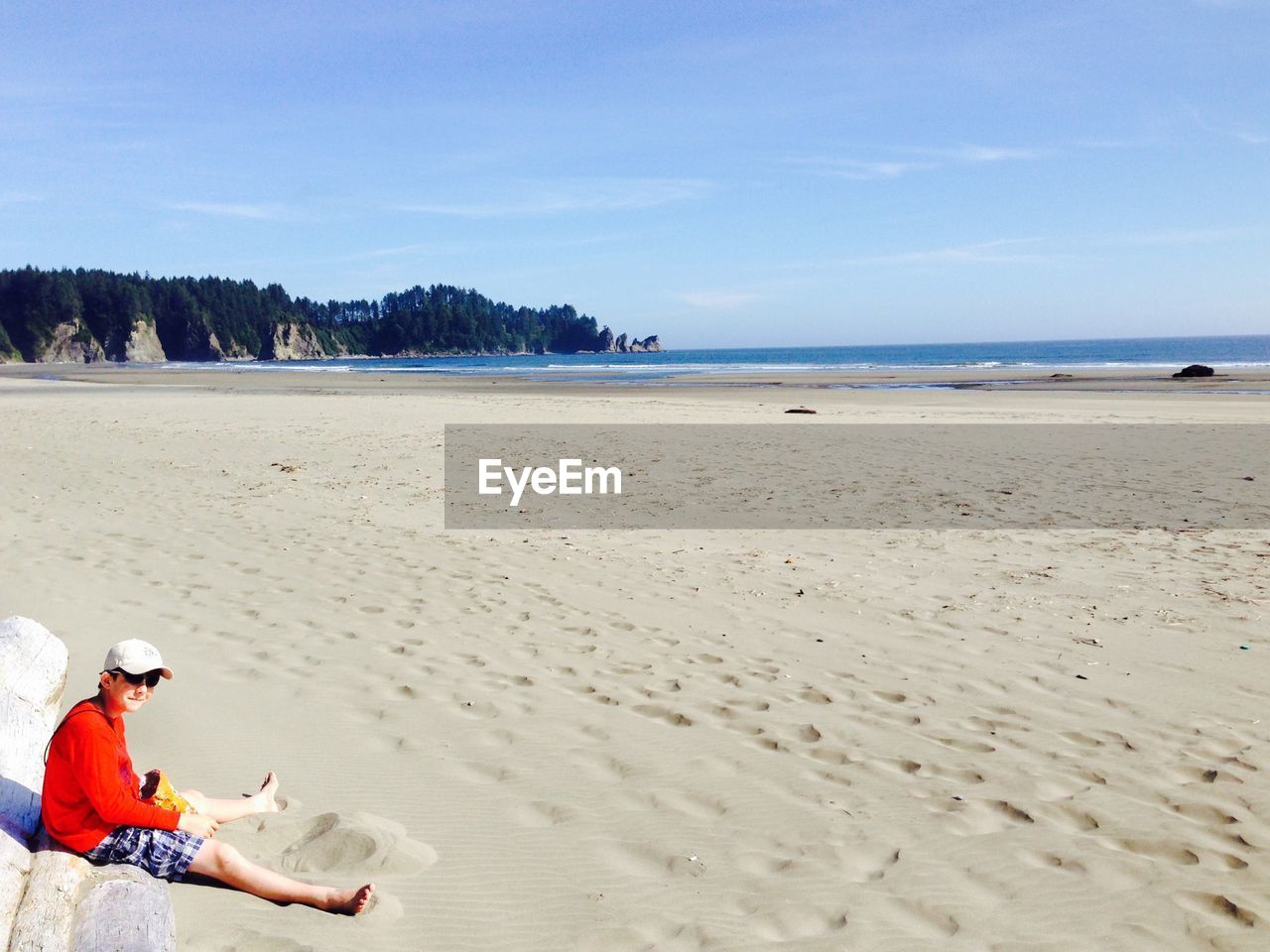 Boy sitting on sand at beach against sky