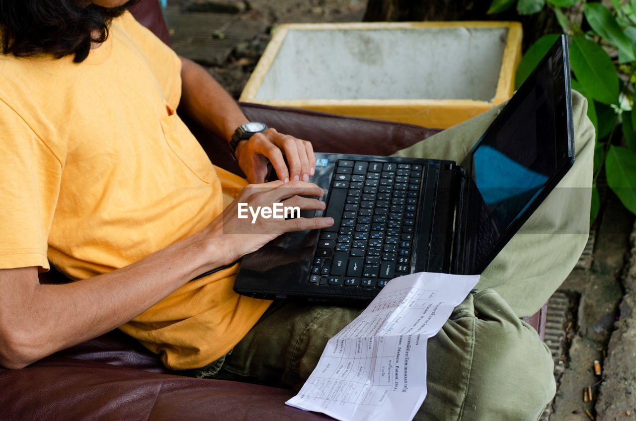 Midsection of man using laptop while sitting on seat