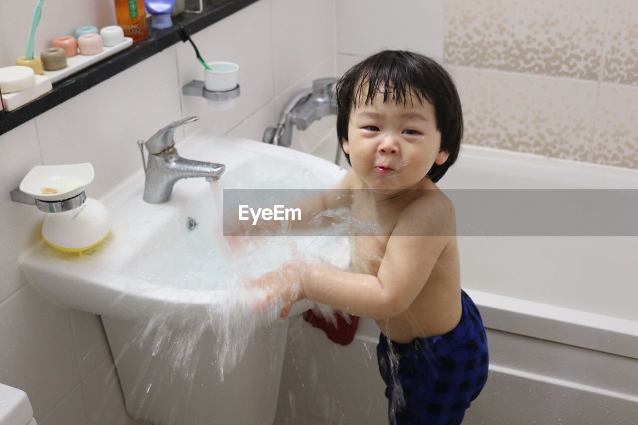 Portrait of cute boy playing in running water on wash bowl