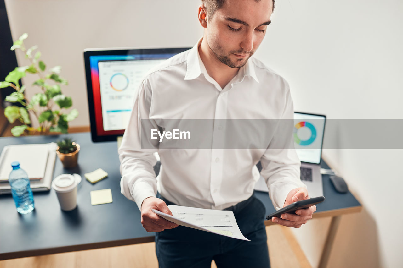 Businessman working in office using smartphone and computer standing at desk. entrepreneur at work