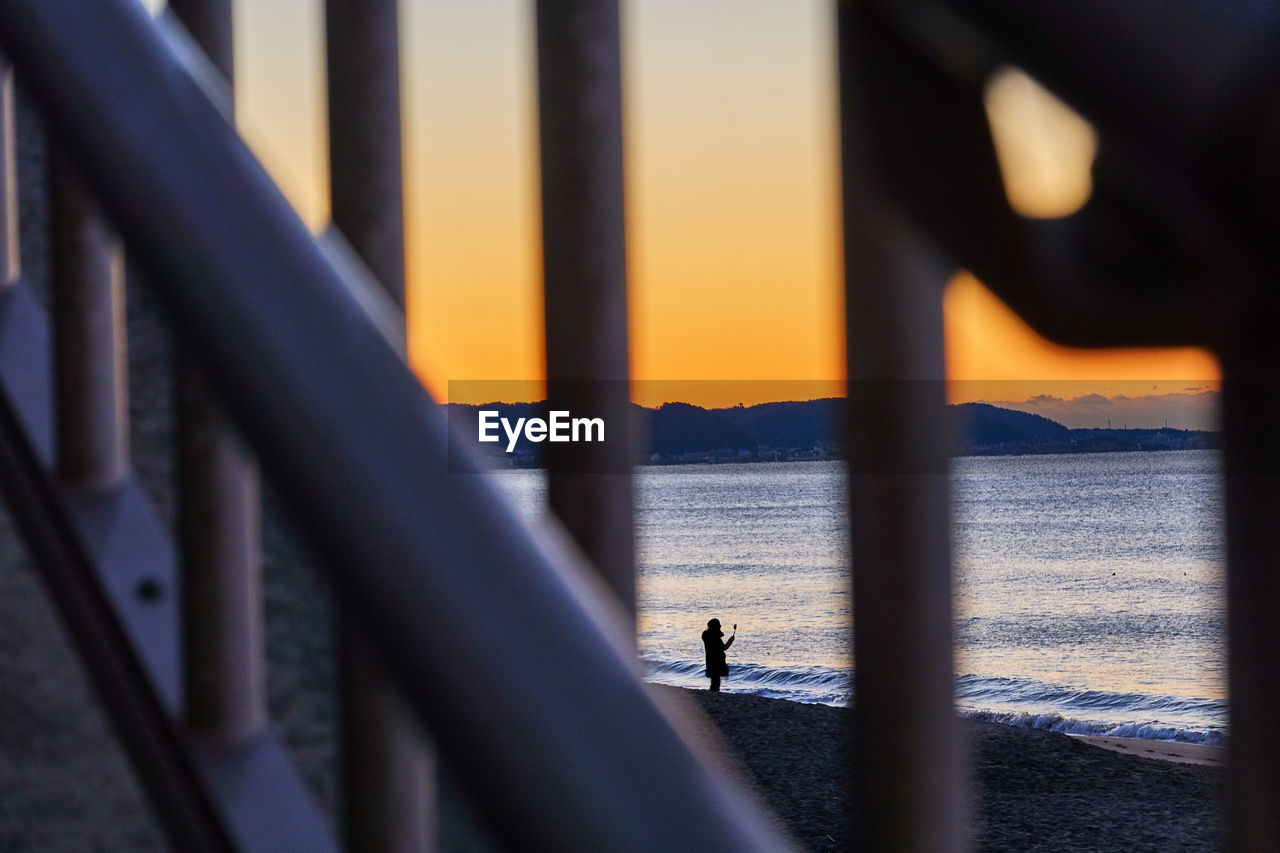 Silhouette people standing by railing against sea during sunrise