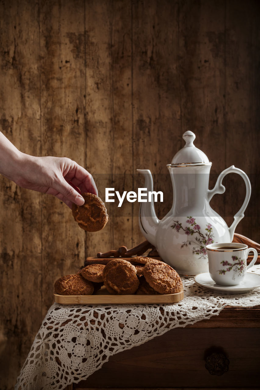 Hand taking homemade cookies with coffee in vintage dishware