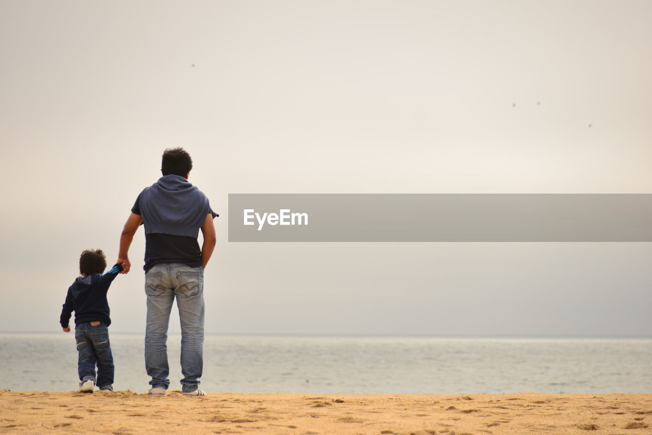 Rear view of father and son at beach against clear sky