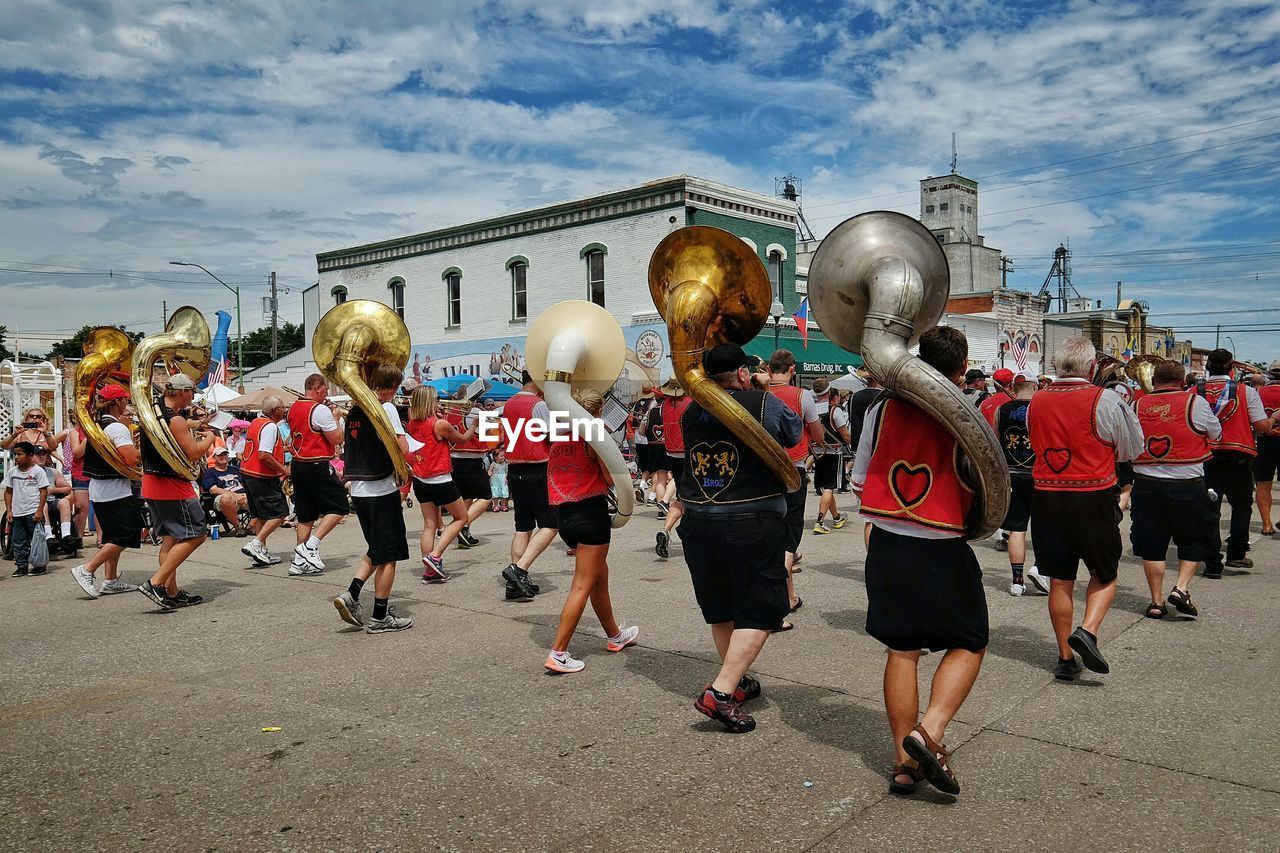 People marching with sousaphone on street against cloudy sky