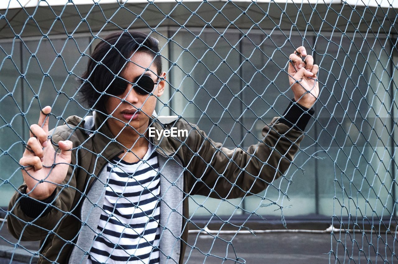 Portrait of young man looking through chainlink fence