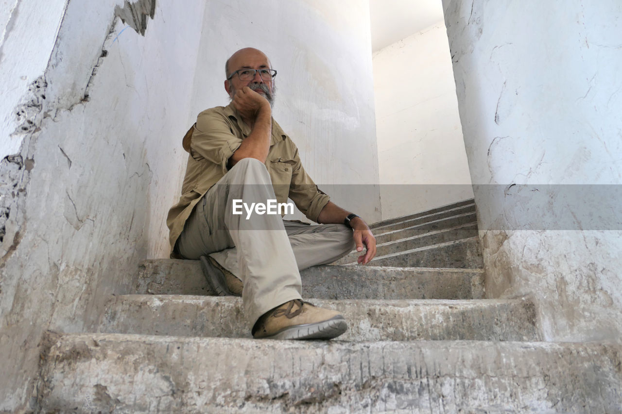 Senior man sitting on staircase against wall