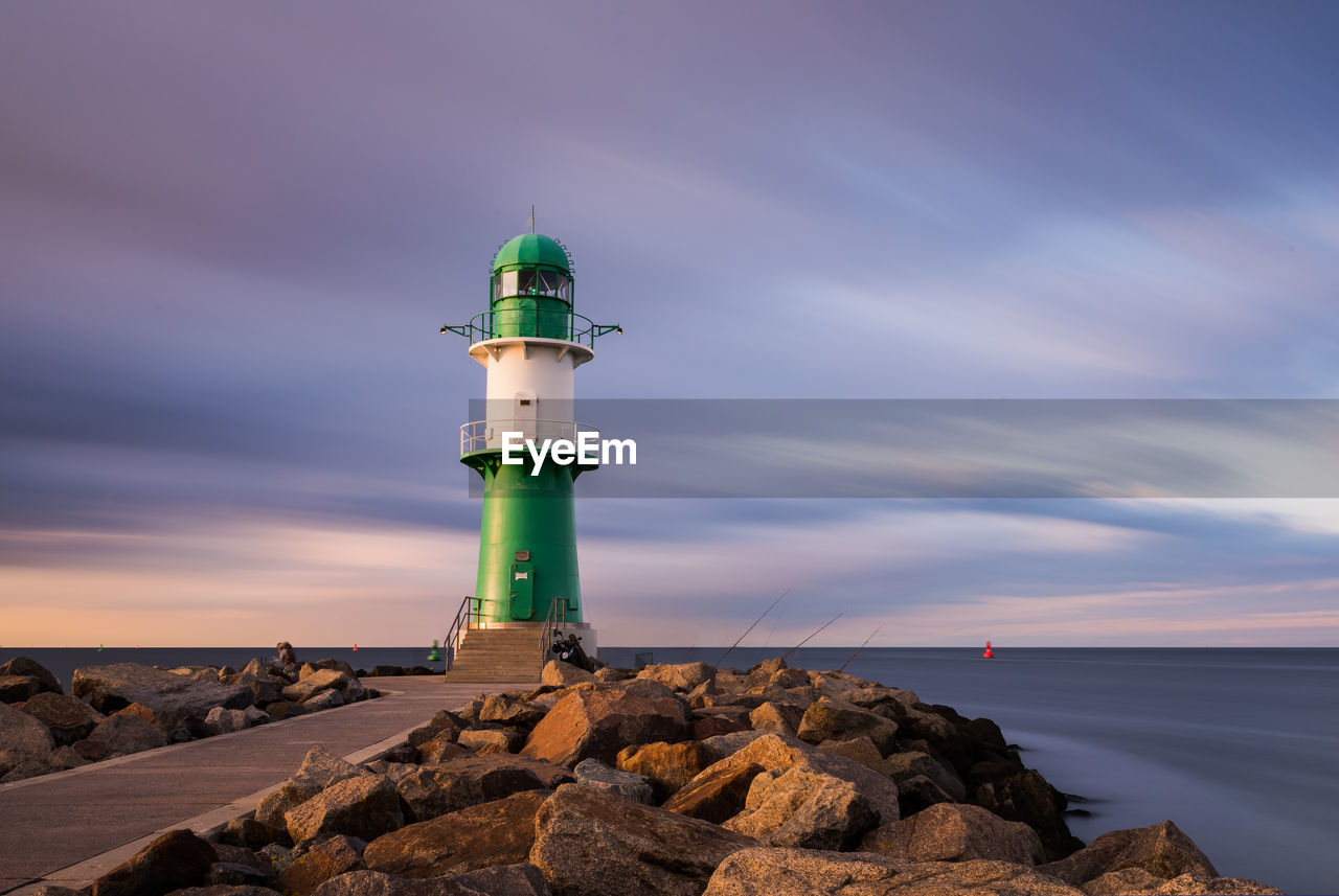 Lighthouse by sea against sky during sunset