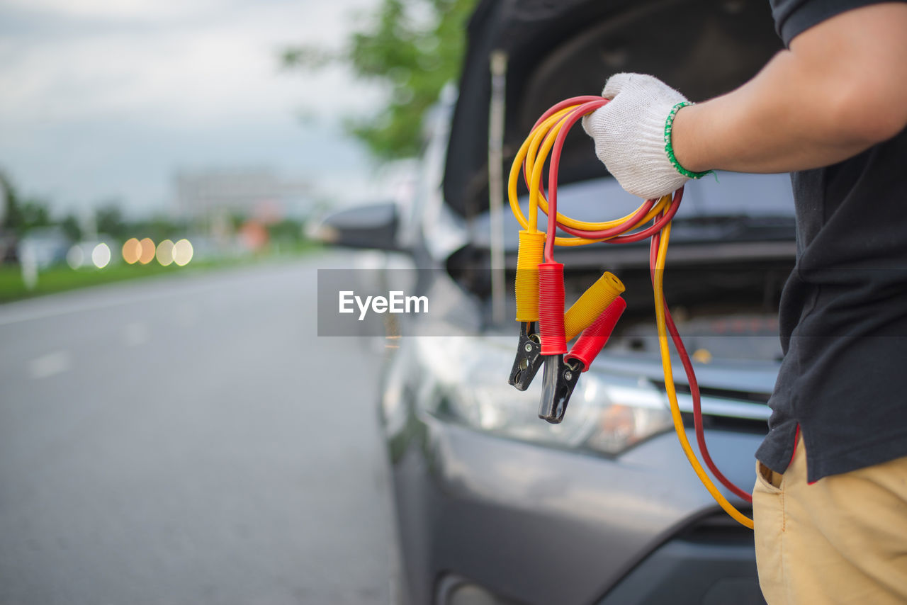 Midsection of man holding cable while standing by car