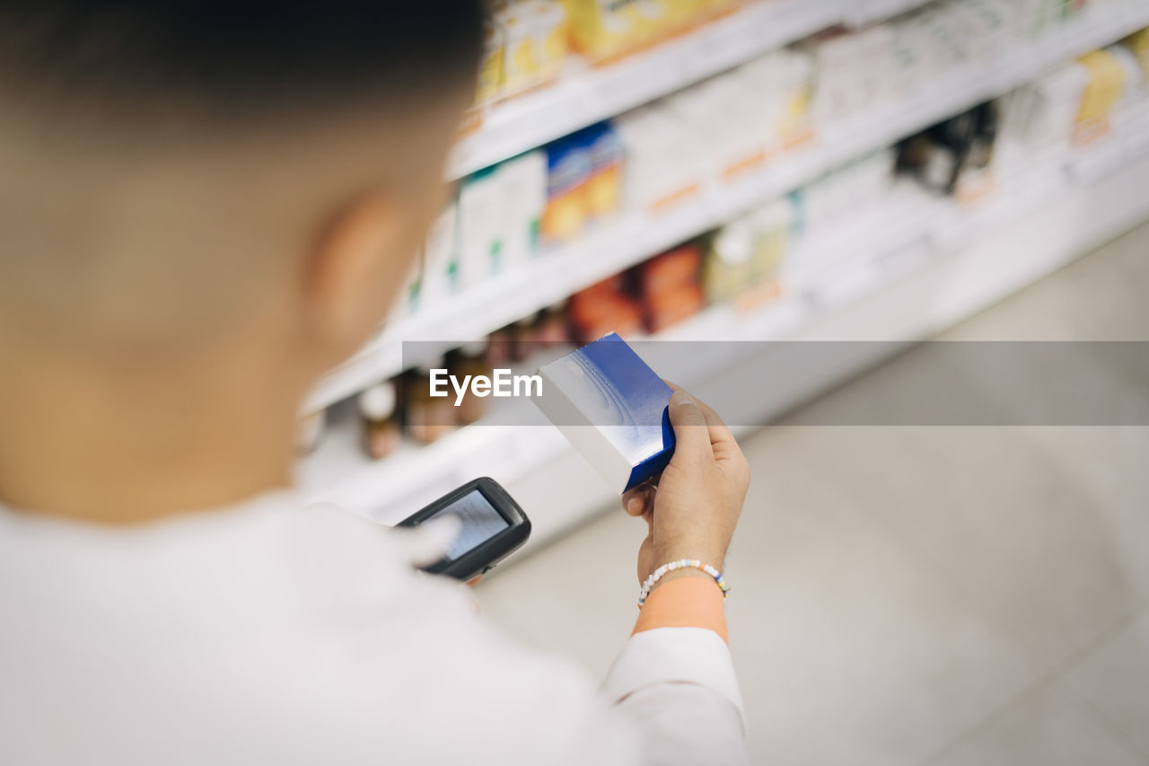 High angle view of male pharmacist using bar code reader on medicine at store