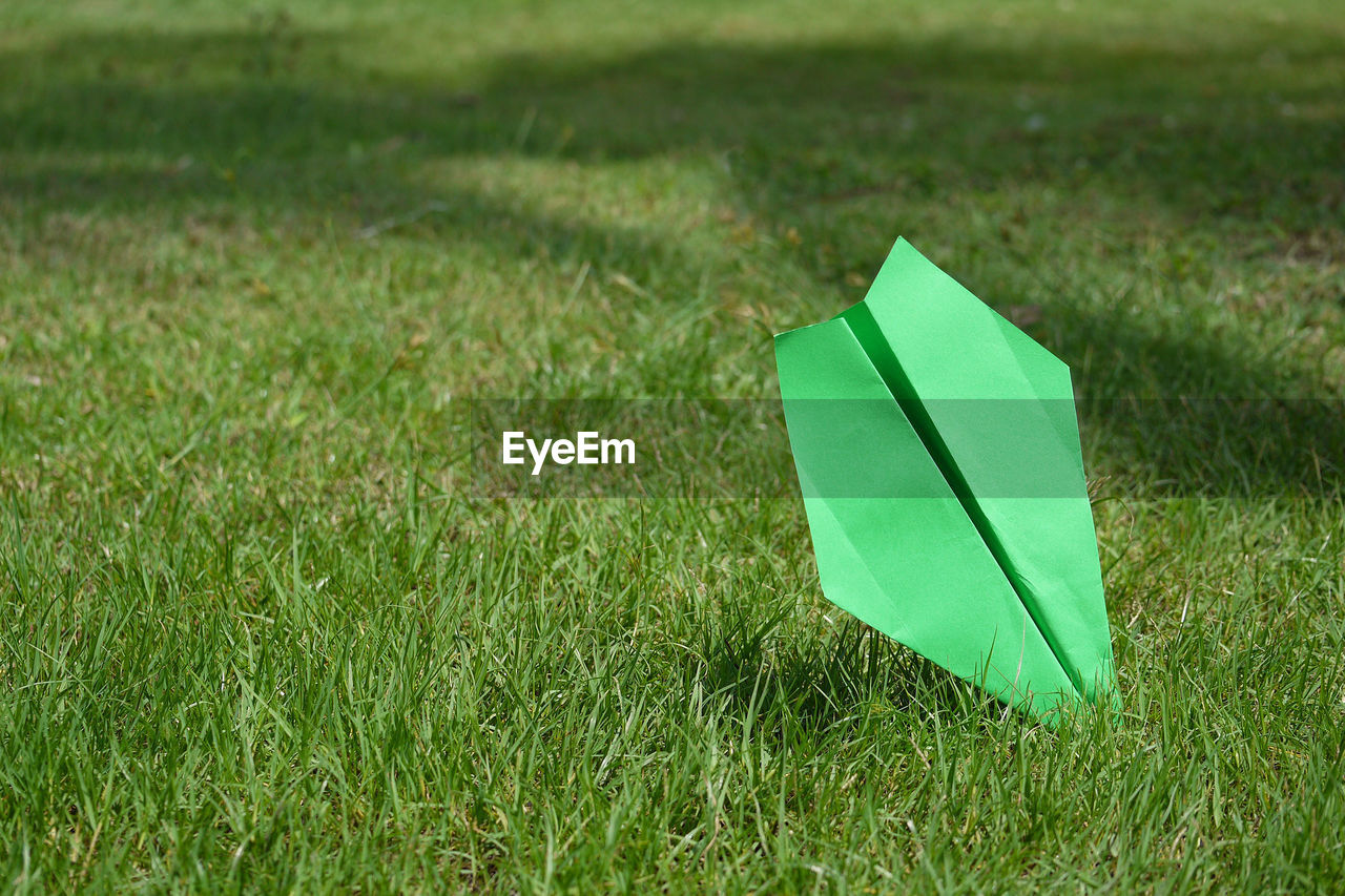 Green paper airplane on grassy field