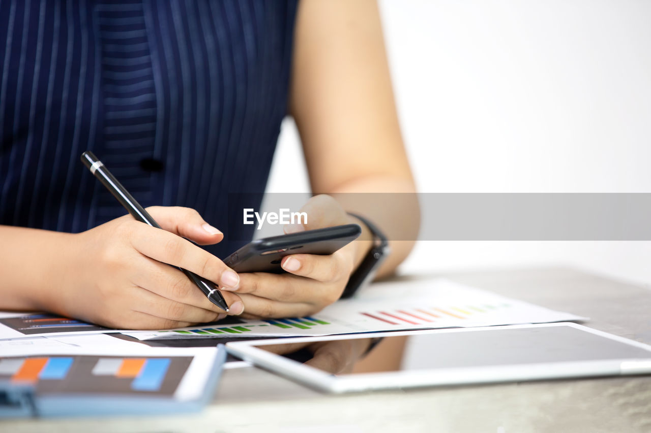 Midsection of businesswoman using phone while working over graph on table