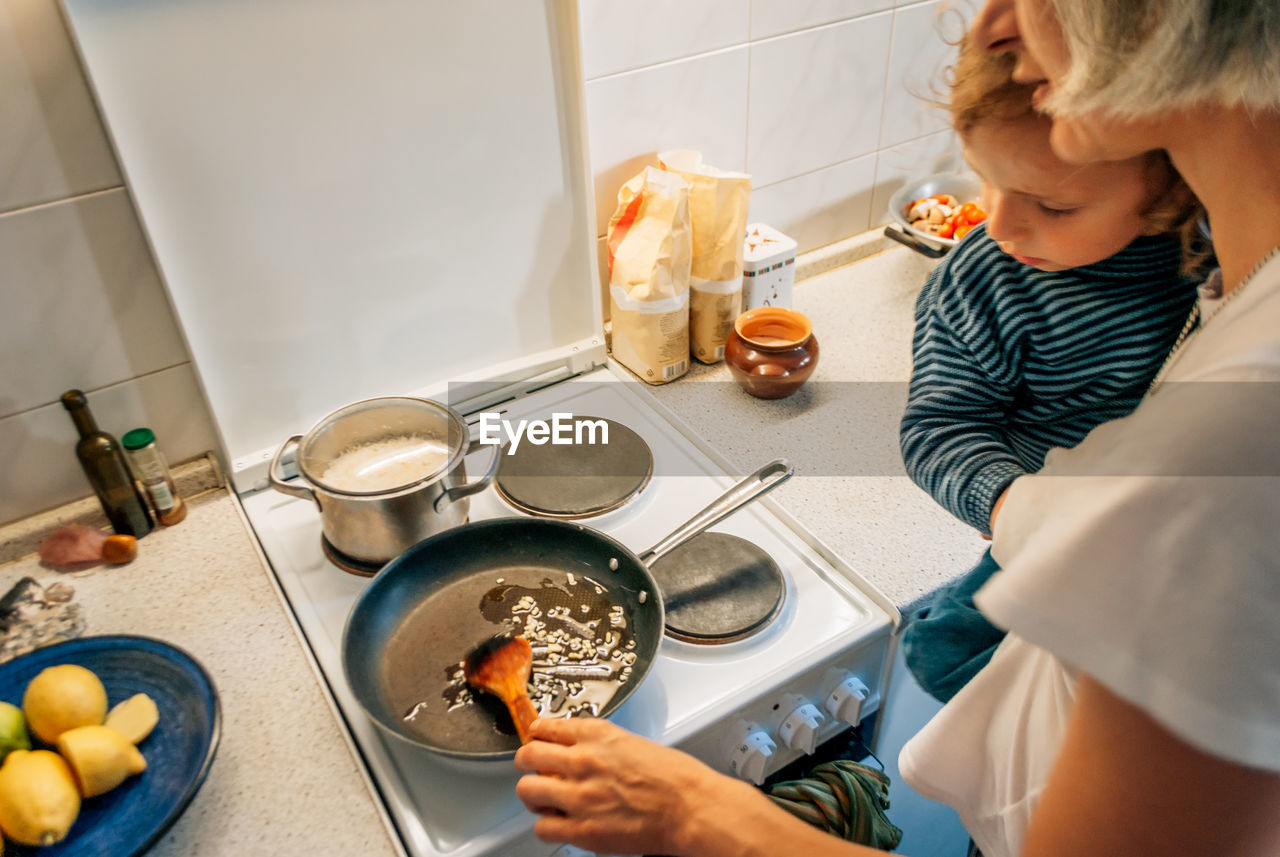 A woman cooks dinner at home with a child in her arms