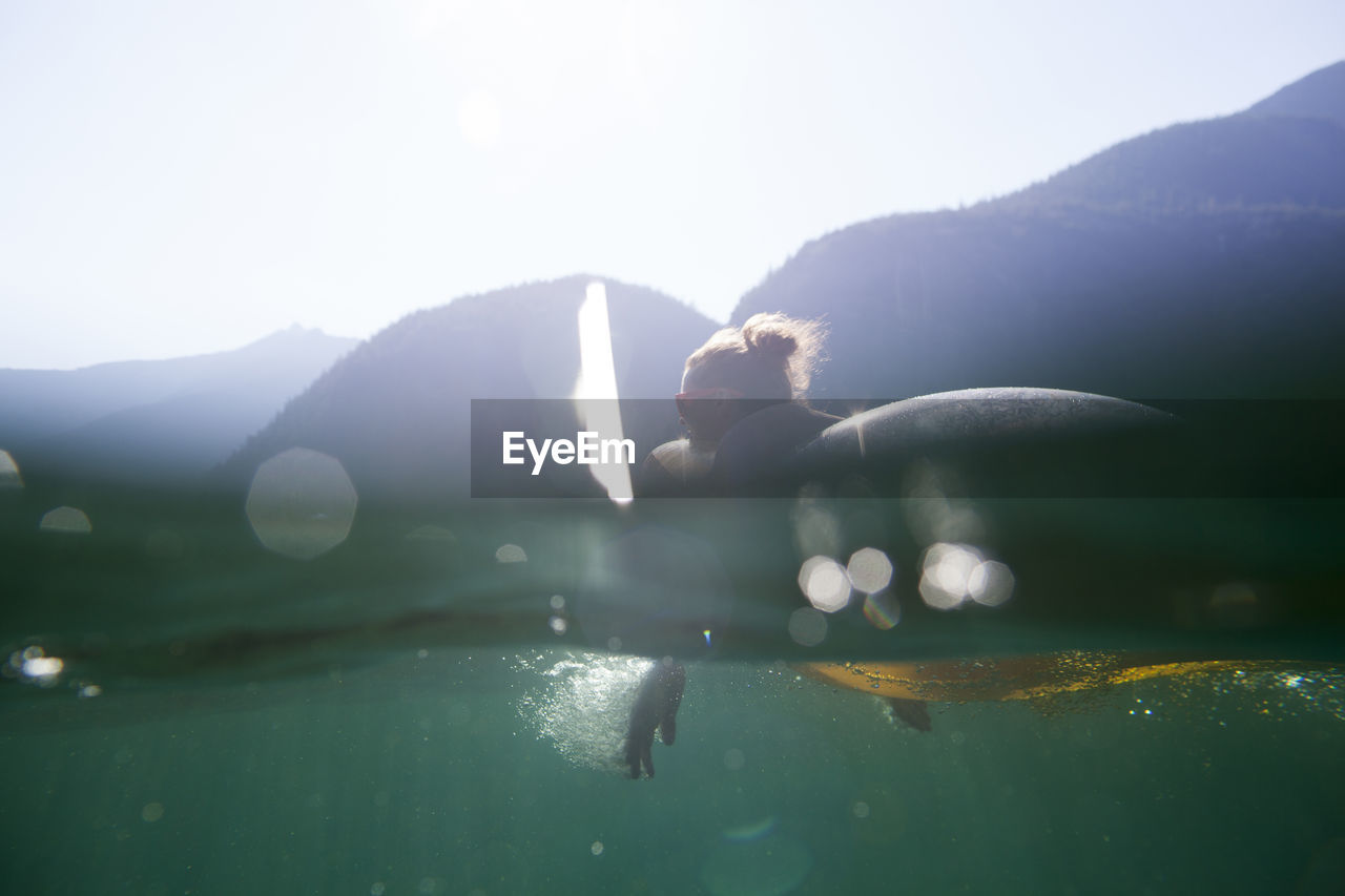 Woman lying on pool raft in lake against mountains during summer