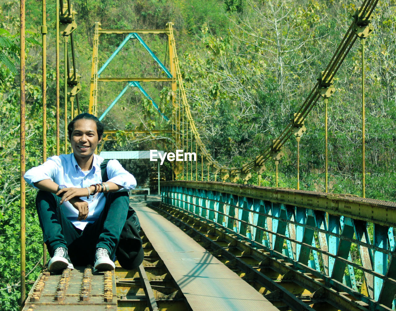 full length of smiling young woman standing on footbridge