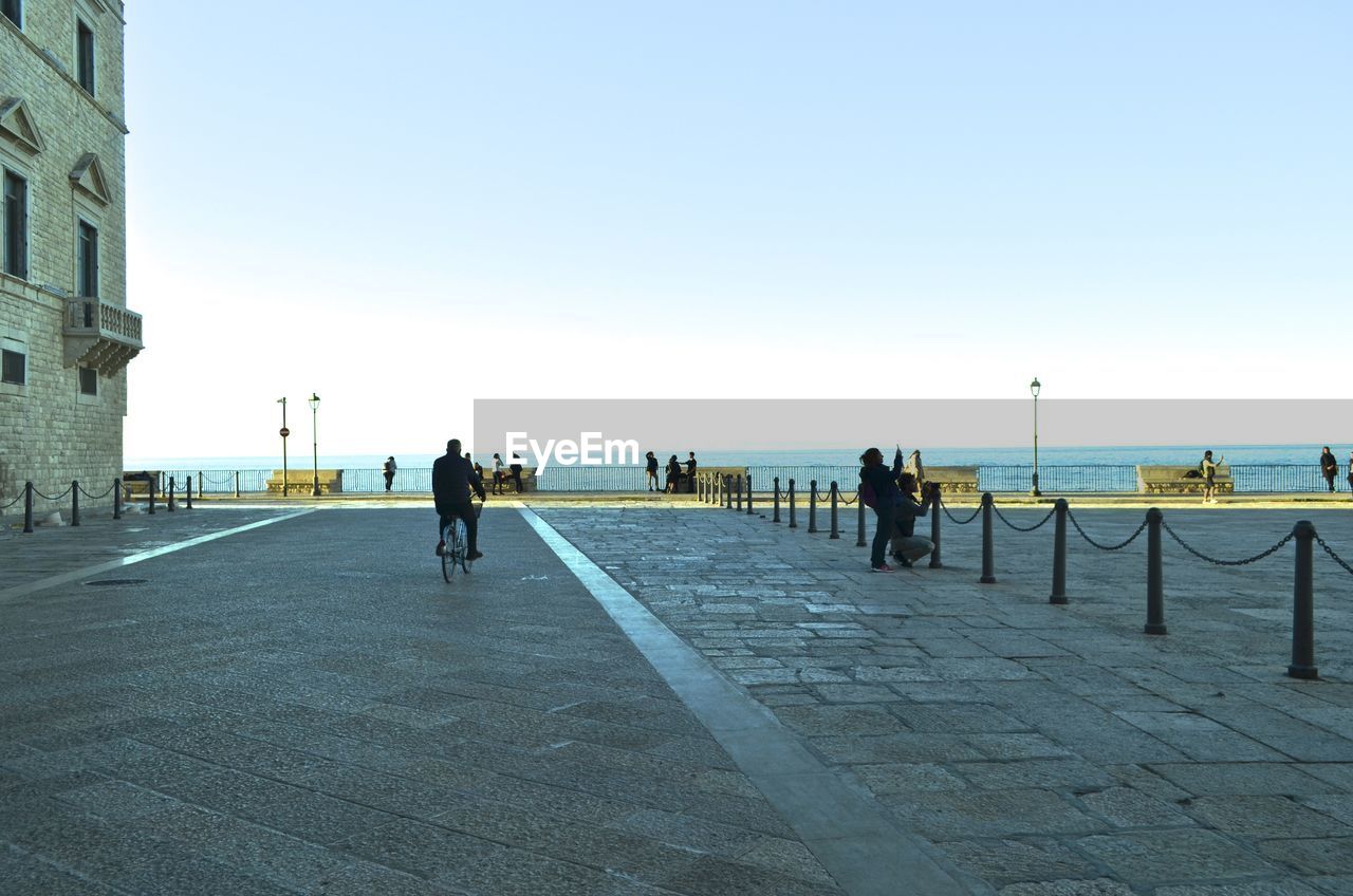 PEOPLE ON FOOTPATH BY SEA AGAINST CLEAR SKY