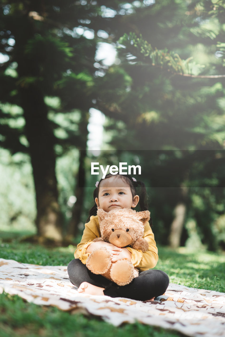 Cute girl with teddy bear sitting on grass at park