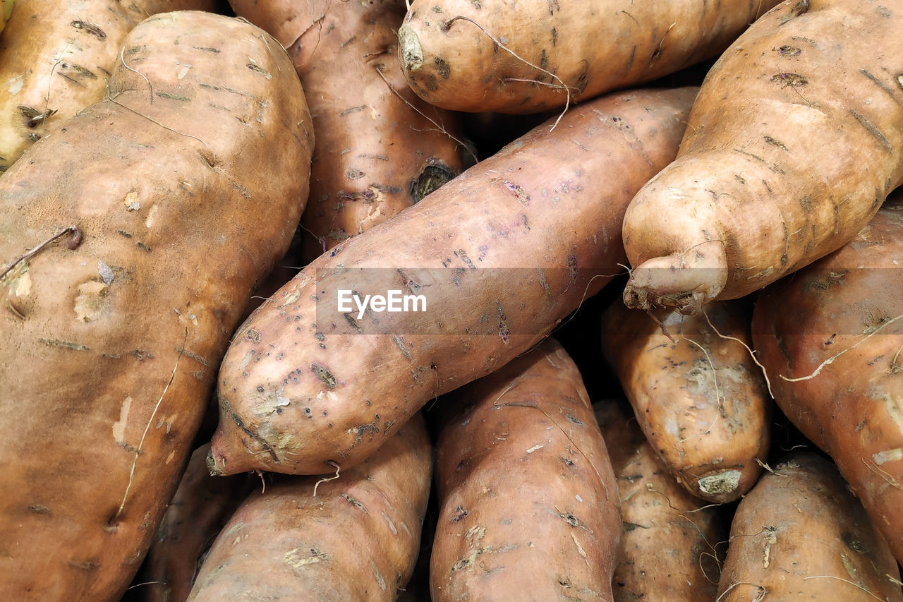 Close-up on a stack of sweet potatoes on a market stall.
