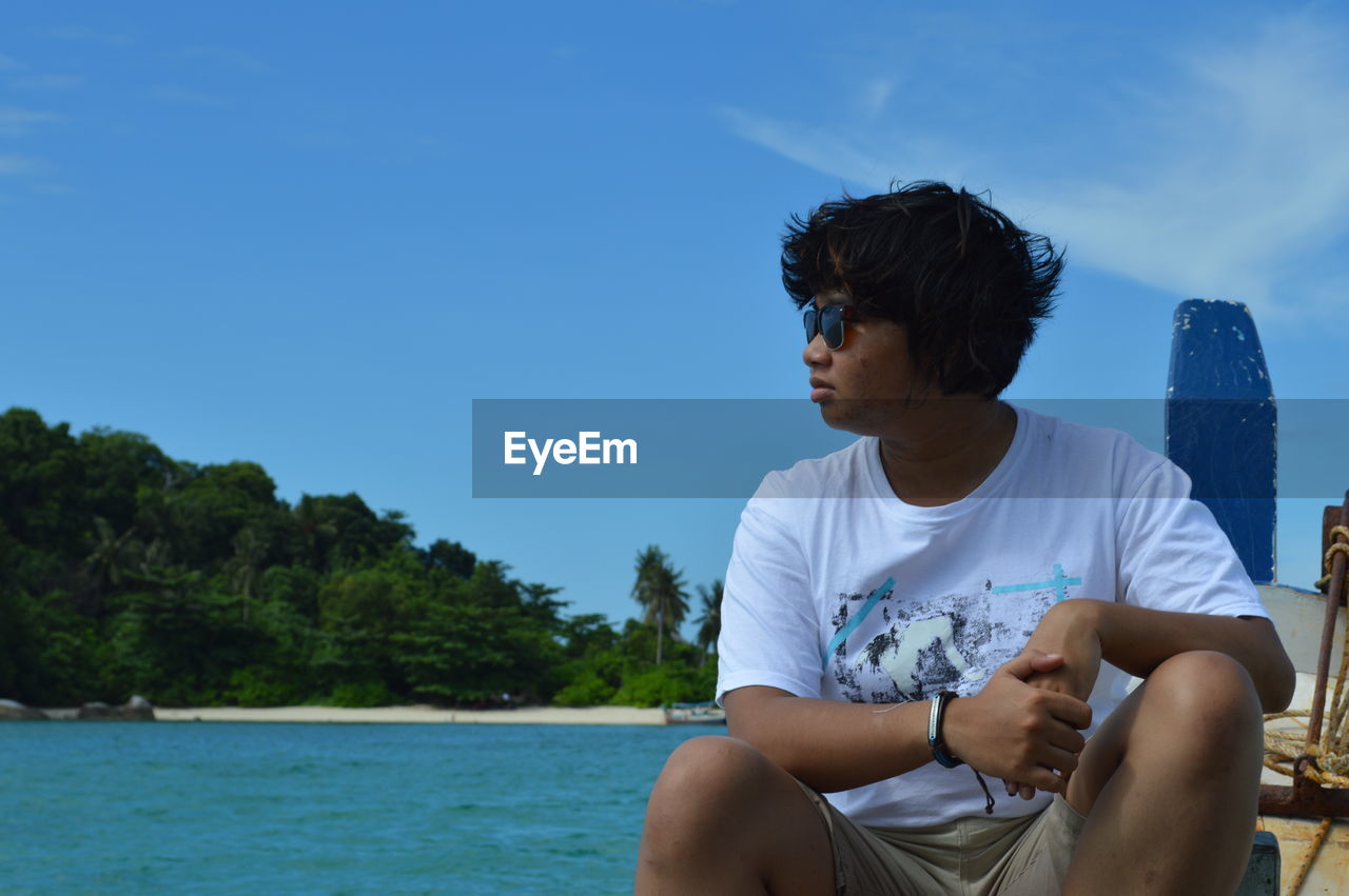 Young man wearing sunglasses sitting on boat at belitung island against blue sky