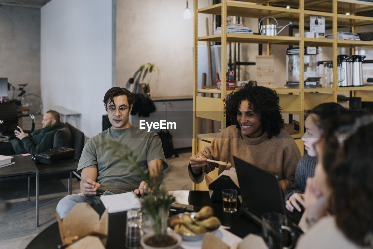 Smiling business colleagues discussing while having lunch at table in creative office