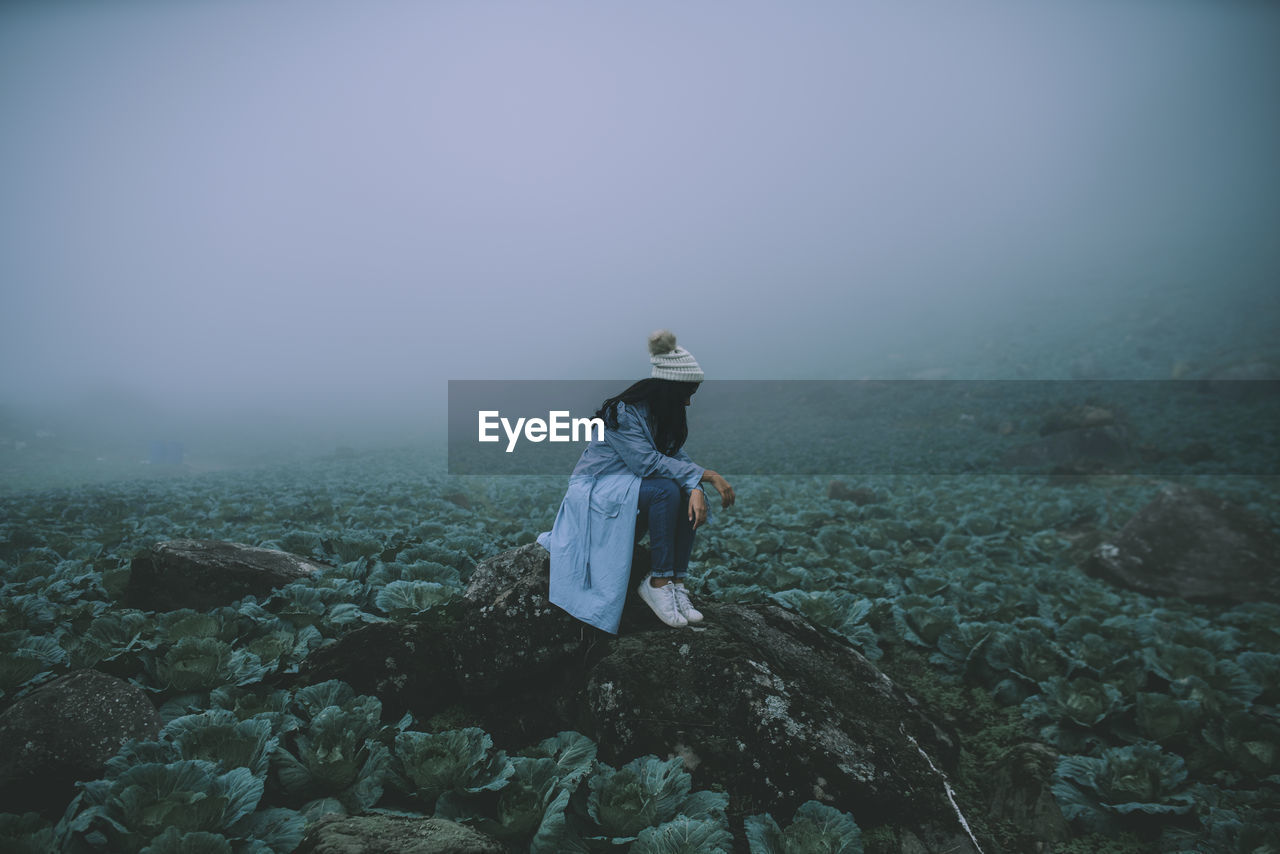 rear view of woman standing on rock against sky