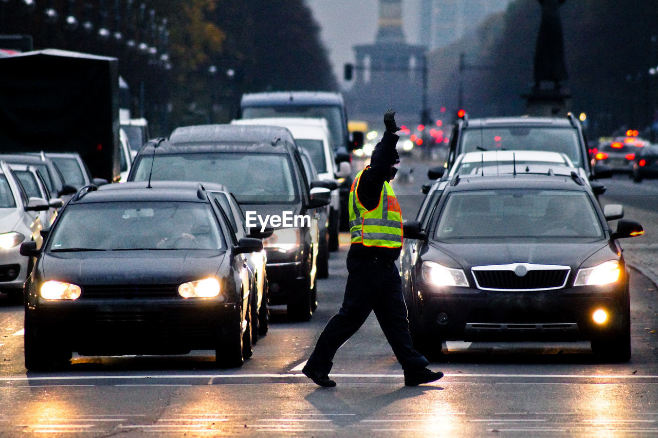 Traffic cop walking by illuminated cars on city street at dusk