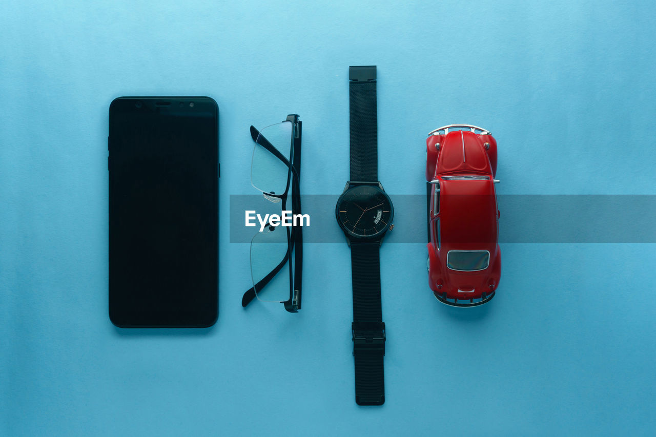 Directly above shot of gadget, eye-glasses, watch and toys on table against blue background