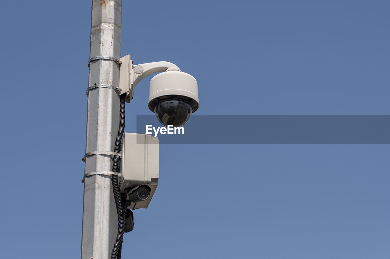 Low angle view of security camera against clear blue sky during sunny day