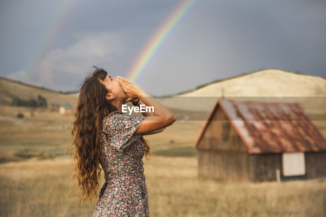 Optical illusion of rainbow coming out from mouth of woman standing in field