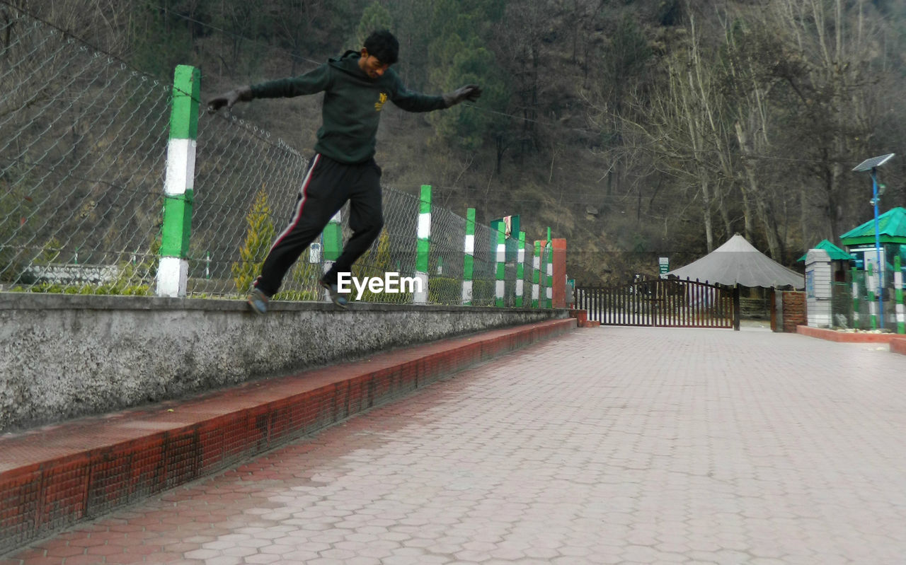 Full length of young man jumping on footpath