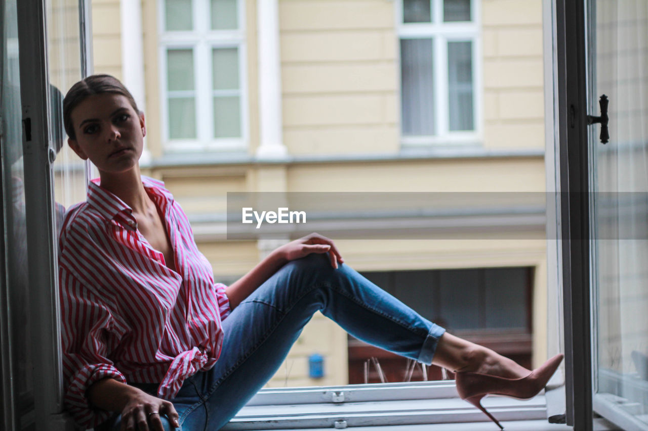 Full length of woman sitting on window of building