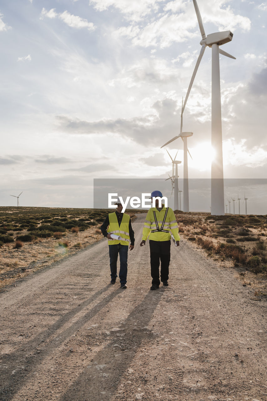 Technician and colleague discussing walking on dirt road at wind turbines
