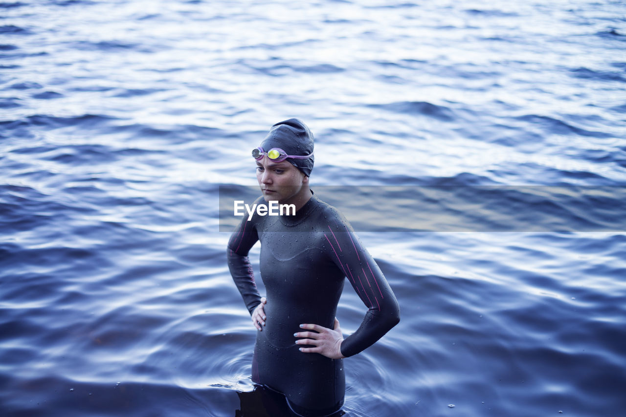 High angle view of thoughtful swimmer standing with hand on hip in lake