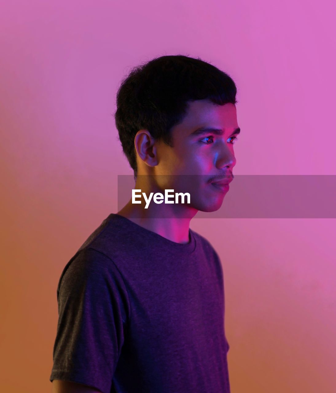 Portrait of young man looking away against pink background