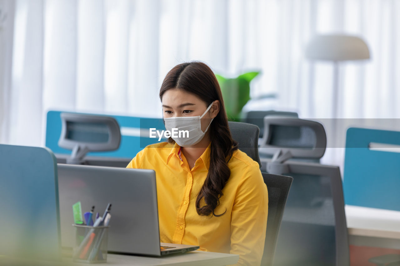 Woman wearing mask while sitting by laptop at table