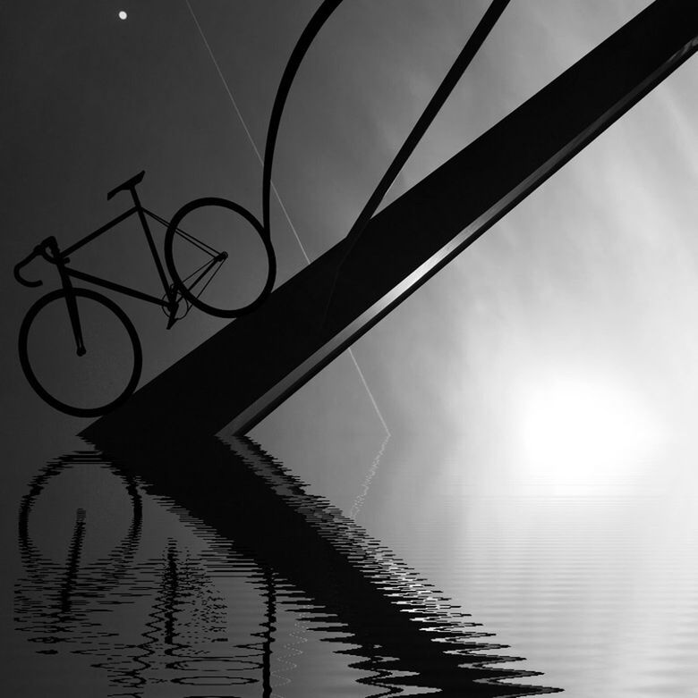 Digital composite image of silhouette bicycle on pole on water