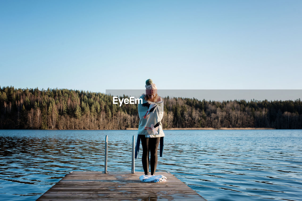 Woman standing wrapped in a towel on a pier after cold water ice swim