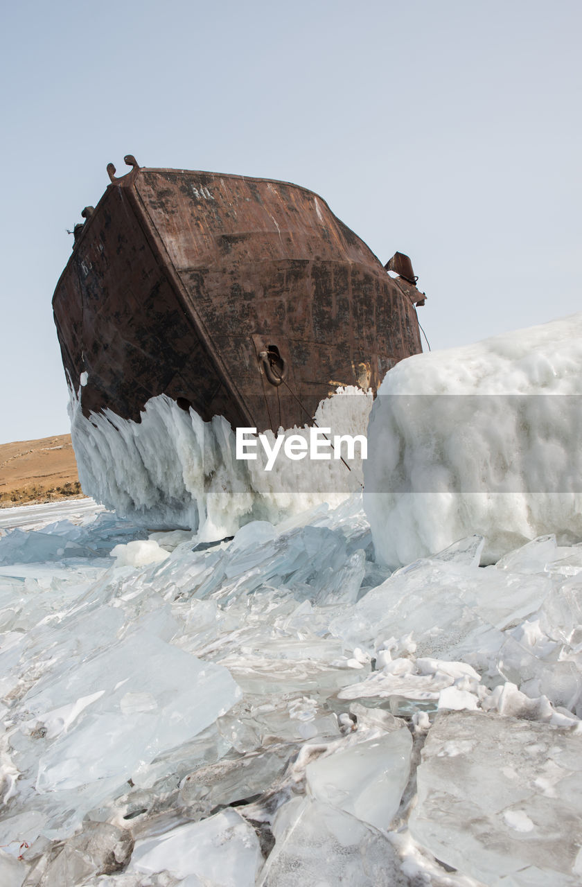Abandoned boat at frozen beach against clear sky