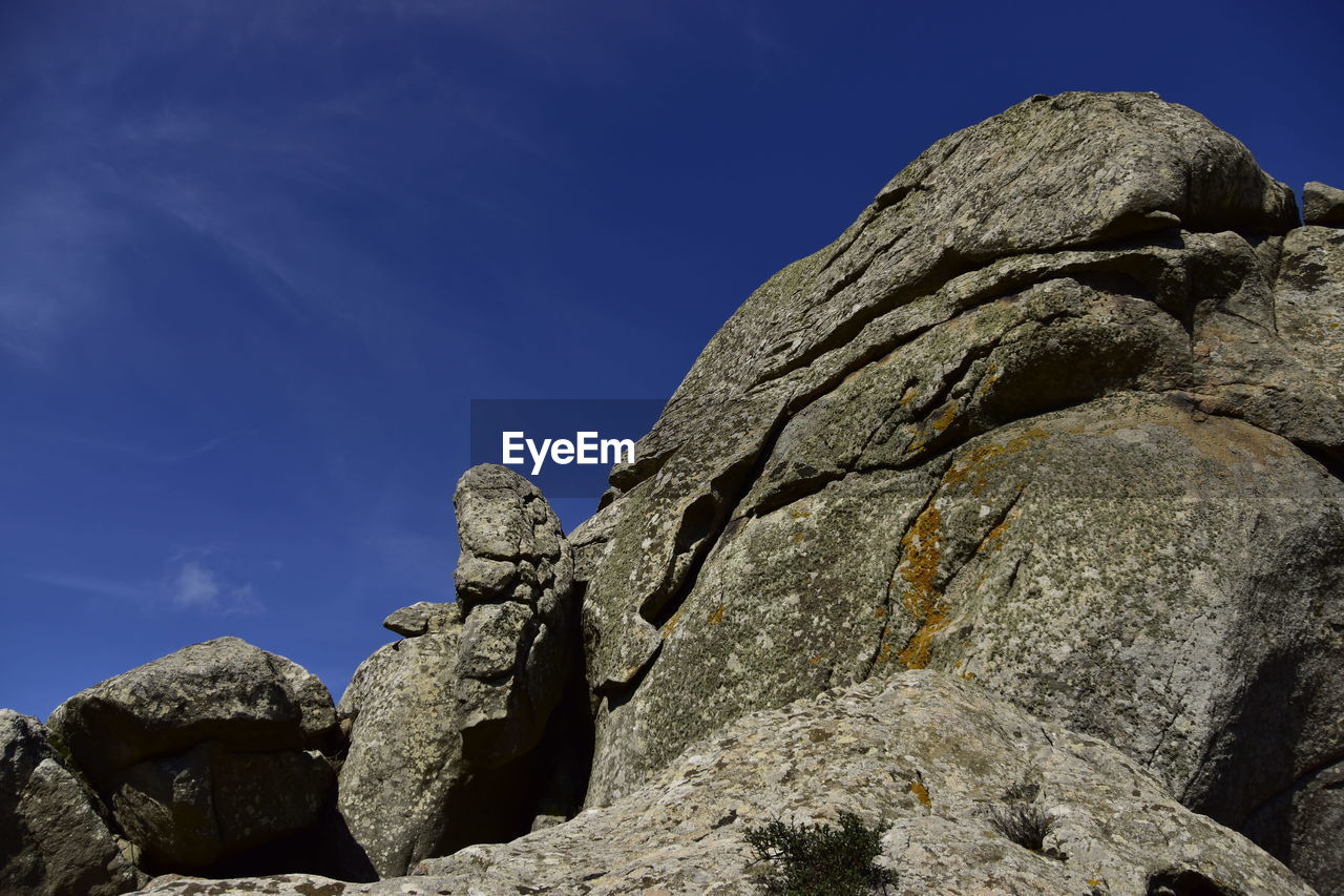 LOW ANGLE VIEW OF STATUE AGAINST ROCK FORMATION AGAINST BLUE SKY