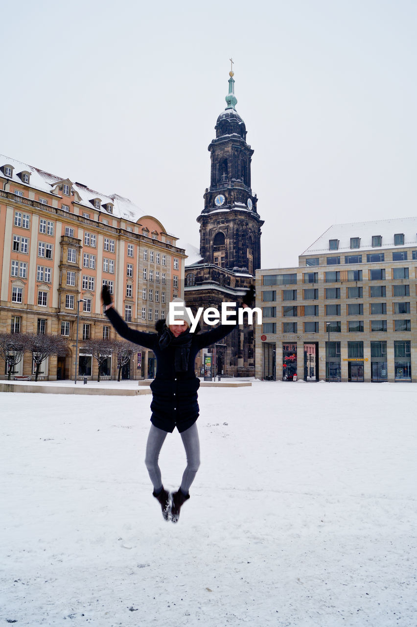 Happy woman jumping at market square against kreuzkirche church during winter