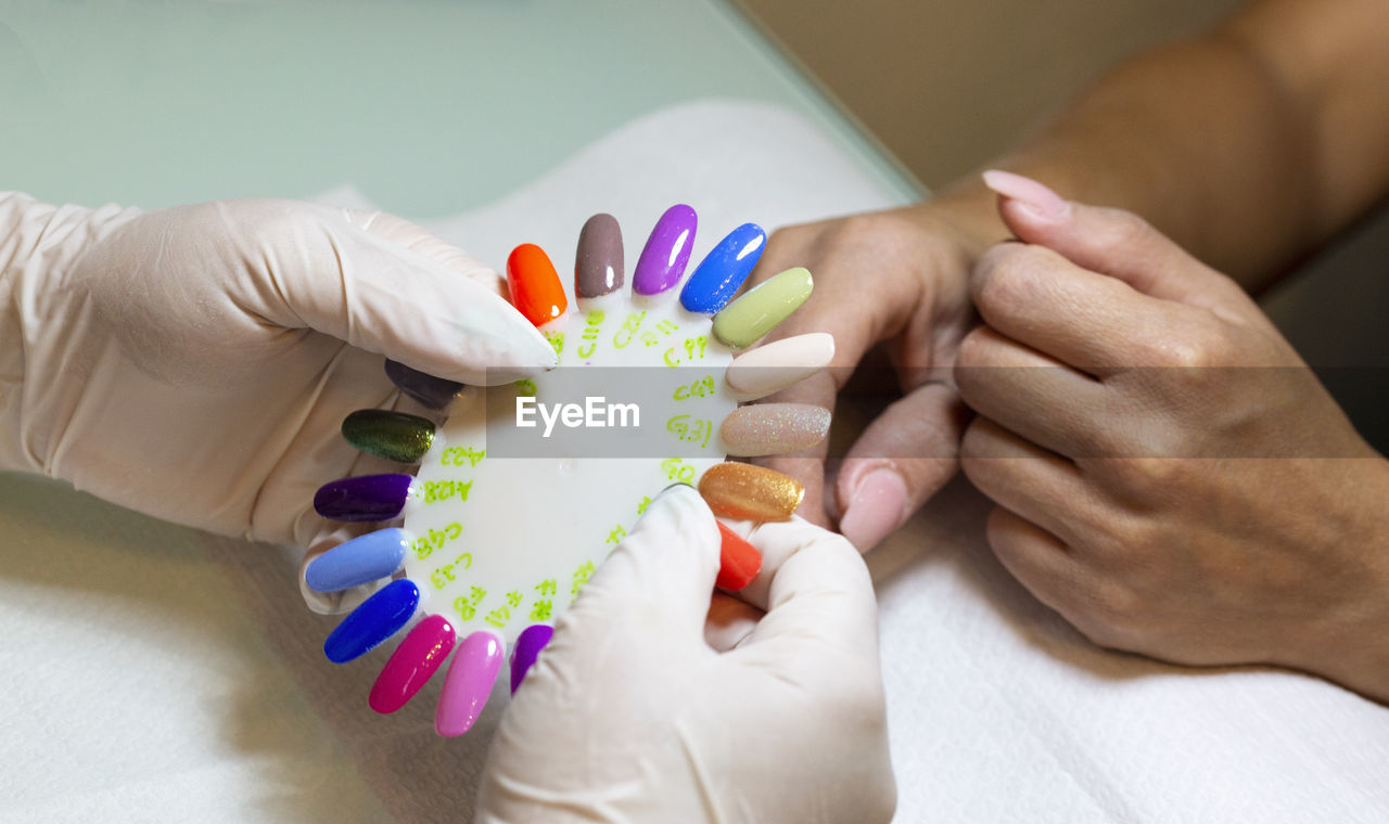 Cropped hands of beautician showing colorful nail arts to woman