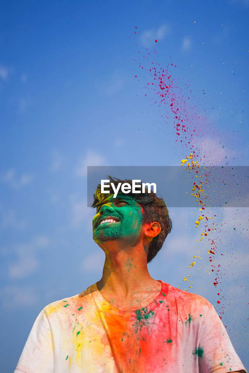 Low angle view of man playing holi against sky