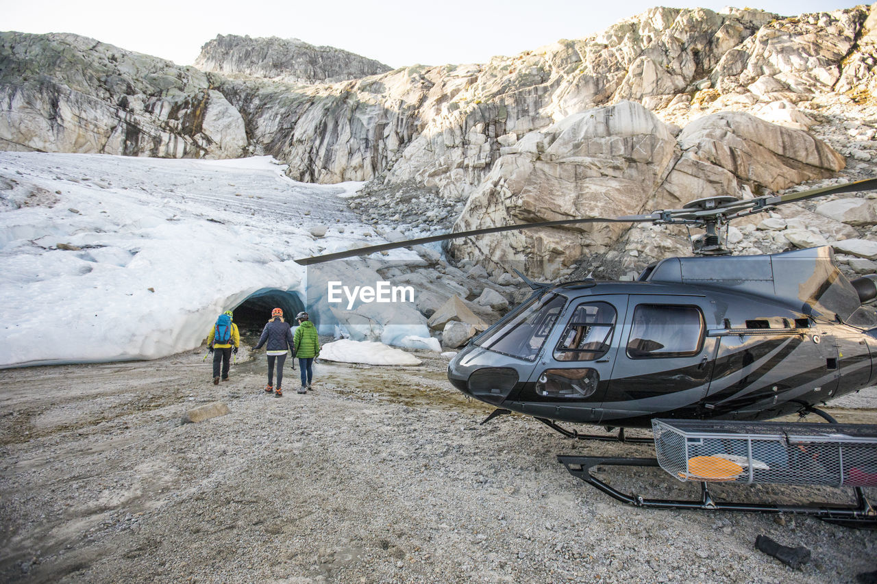 A mountain guide approaches a glacial ice cave with tour clients.